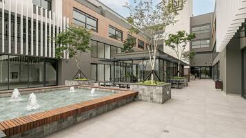 Un patio con fuente ornamental, zonas de estar y edificios modernos con amplios ventanales.