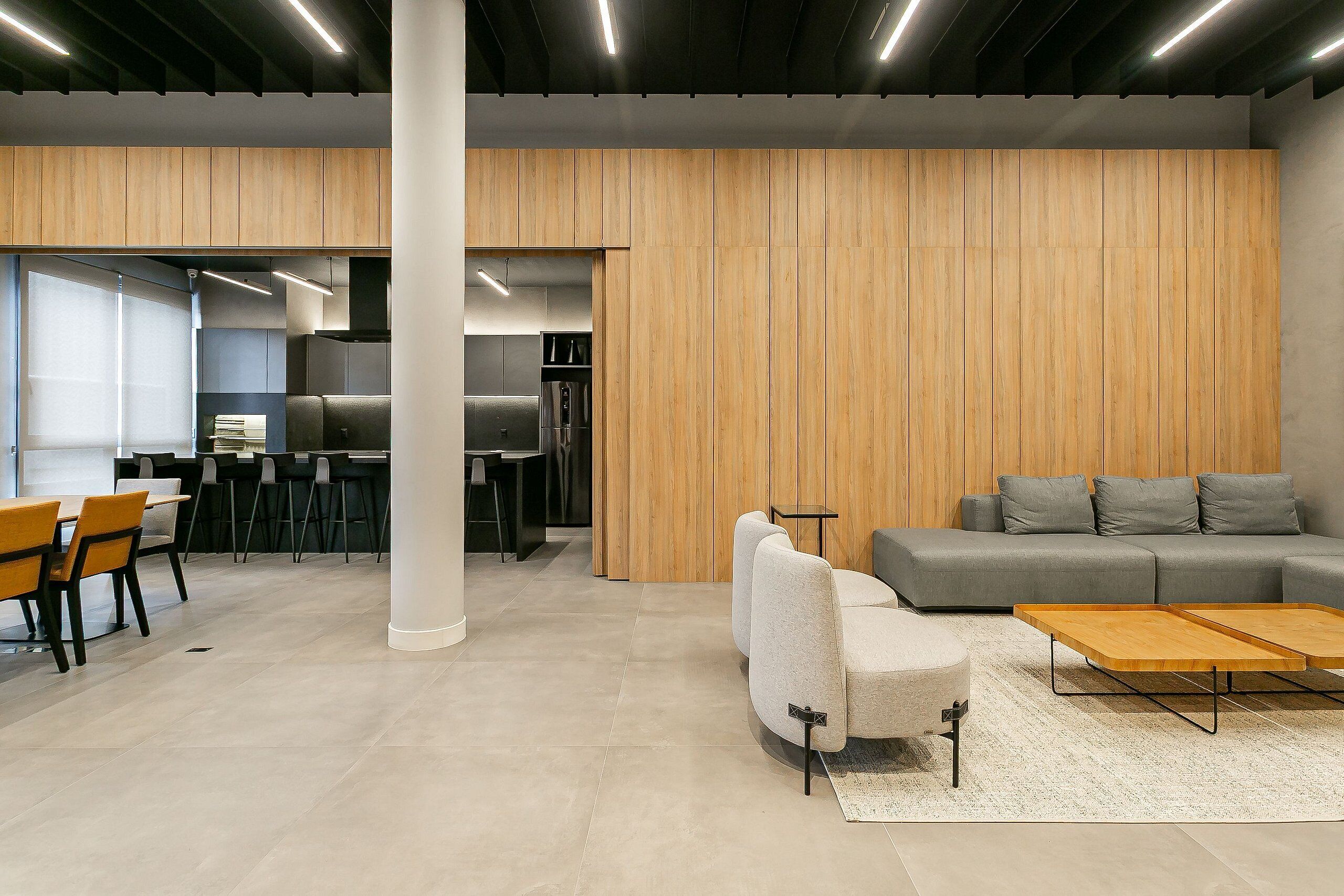 Un interior moderno con un sofá gris, paneles de madera y una zona de comedor con sillas y mesas.