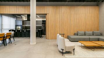 Un interior moderno con un sofá gris, paneles de madera y una zona de comedor con sillas y mesas.