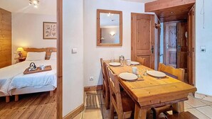 Una habitació amb un llit de fusta, una taula de menjador preparada per a quatre persones, un mirall i una porta de fusta.