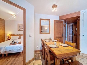 Ein Zimmer mit einem hölzernen Bett, einem Esstisch für vier Personen, einem Spiegel und einer Holztür.