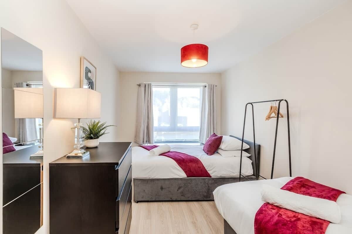 Una habitación de hotel moderna con dos camas, un escritorio, un espejo y una ventana con cortinas.