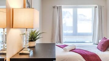 Une chambre d’hôtel avec un lit, un bureau doté d’une lampe, une plante en pot et une fenêtre avec des rideaux.