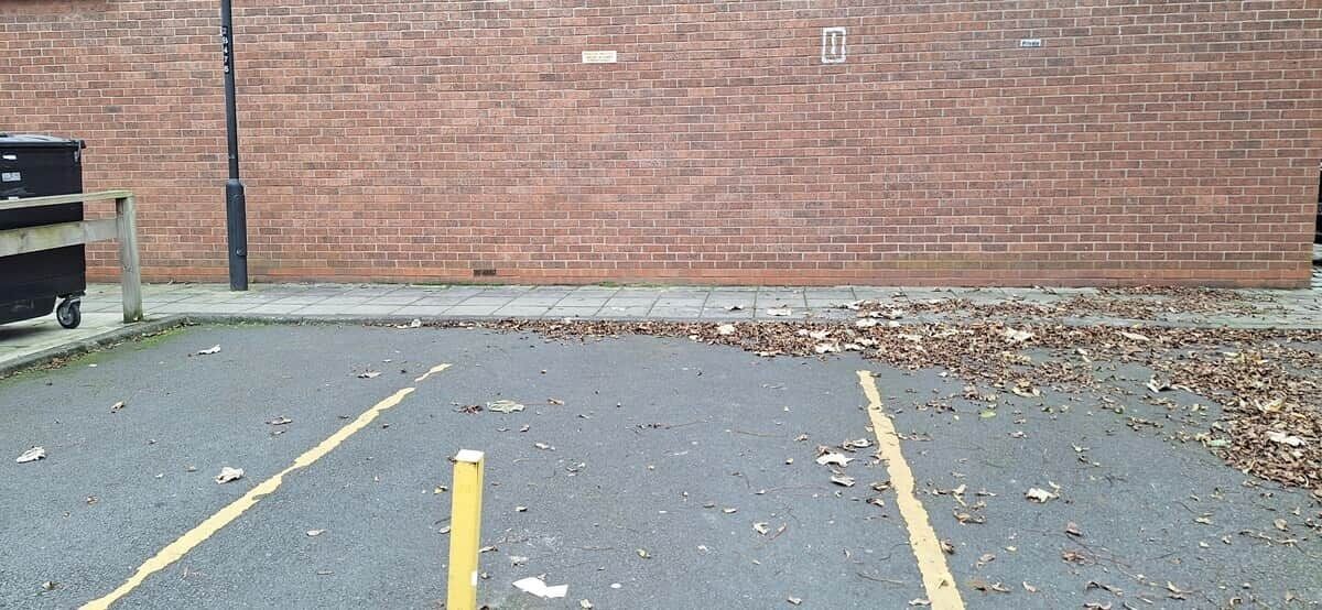 Um estacionamento com muro de tijolos e um contentor de lixo.