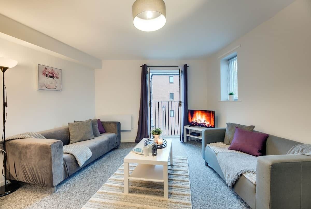 Un salon comprenant deux canapés, une table basse, un lampadaire, une cheminée et une fenêtre avec des rideaux.