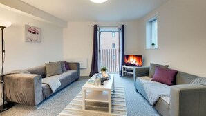 A living room with two sofas, a coffee table, a floor lamp, a fireplace, and a window with curtains. - Spacious 3 Bed City Centre Apartment, Free Parking, sleeps 5 (Newcastle upon Tyne)