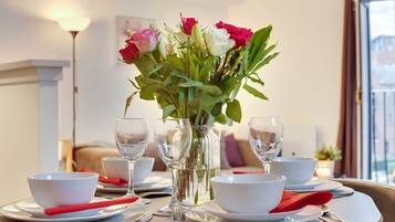 Une table à manger dressée avec des bols blancs, des serviettes rouges et de la vaisselle transparente, et un vase de fleurs placé au centre.