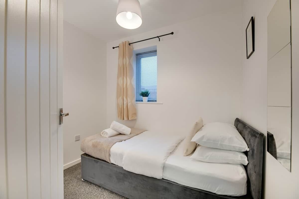 A bedroom with a bed, a window with blinds, a hanging curtain, and a ceiling light fixture.