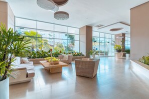 Eine großzügige Lobby mit großen Fenstern, einer Couch, einem Korbstuhl und Topfpflanzen.