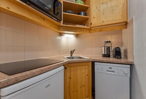 A compact kitchen with a dishwasher, a sink, wooden cabinets, and a microwave. - 40m from ski slopes, 2nd floor, fitness, swimming pool, sauna, balcony, tv, ski locker, 35m² (Les Orres)