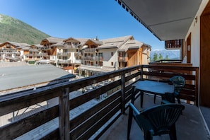 A wooden balcony with a table and chairs, overlooking a row of chalet-style buildings with balconies, set against a mountainous backdrop. - Resort center, 1st floor, fitness, swimming pool, sauna, balcony, tv, ski locker, 35m², Les Orres (Les Orres)