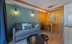 A cozy room with a sofa, dining table, and chairs, wooden walls, and a ceiling with exposed beams. - Resort center, 1st floor, fitness, swimming pool, sauna, balcony, tv, ski locker, 35m², Les Orres (Les Orres)