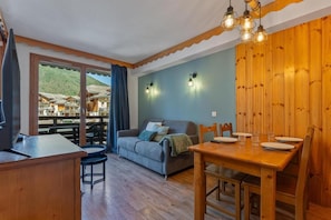 A cozy room with a wooden dining table, a sofa, and a TV. - 40m from ski slopes, 2nd floor, fitness, swimming pool, sauna, balcony, tv, ski locker, 35m² (Les Orres)