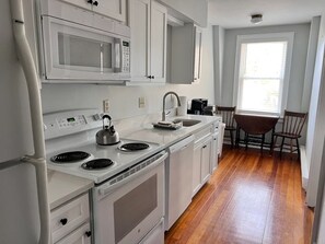 A modern kitchen with white cabinetry, a built-in microwave, a kettle, and a coffee maker. - 2-bedroom apartment in delightful Ogunquit. Walking distance to the Cove (Ogunquit)