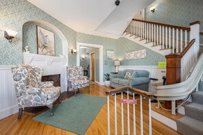 A spacious living area with a fireplace, patterned armchairs, a sofa, and a staircase. - 2-bedroom apartment in delightful Ogunquit. Walking distance to the Cove (Ogunquit)