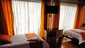 Una habitación de hotel con dos camas, un escritorio, un televisor y una ventana con cortinas.