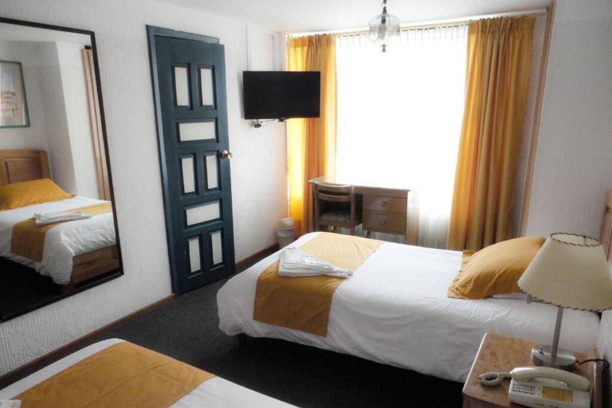 Ett hotellrum med två sängar, ett skrivbord, en stol, en telefon och en tv.