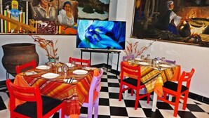 Un comedor con dos mesas, sillas, un televisor y pinturas en las paredes.