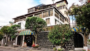 Un edificio de varios pisos con un letrero de hostal, paredes de piedra y un acceso cubierto.