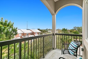 A balcony with a view of houses and trees, a chair with a striped pillow, and a clear blue sky. - Alerio E304 (Miramar Beach)