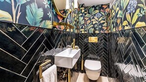 Une salle de bain avec un carrelage disposé en motif « point de Hongrie », un lavabo blanc, des toilettes et un miroir avec un cadre doré.
