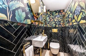 Een badkamer met een visgraat betegeling, een witte wastafel, een toilet en een spiegel met een gouden lijst.
