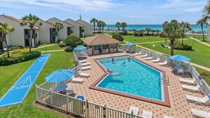 A pool area with a shuffleboard court, lounge chairs, and a view of the ocean. - Blue Surf 1 (Miramar Beach)