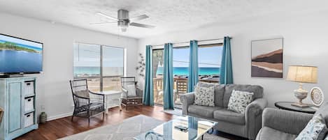 A living room with a glass coffee table, a sofa, a TV, and a view of the ocean.