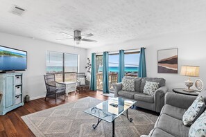 A living room with a glass coffee table, a sofa, a TV, and a view of the ocean. - Blue Surf 1 (Miramar Beach)