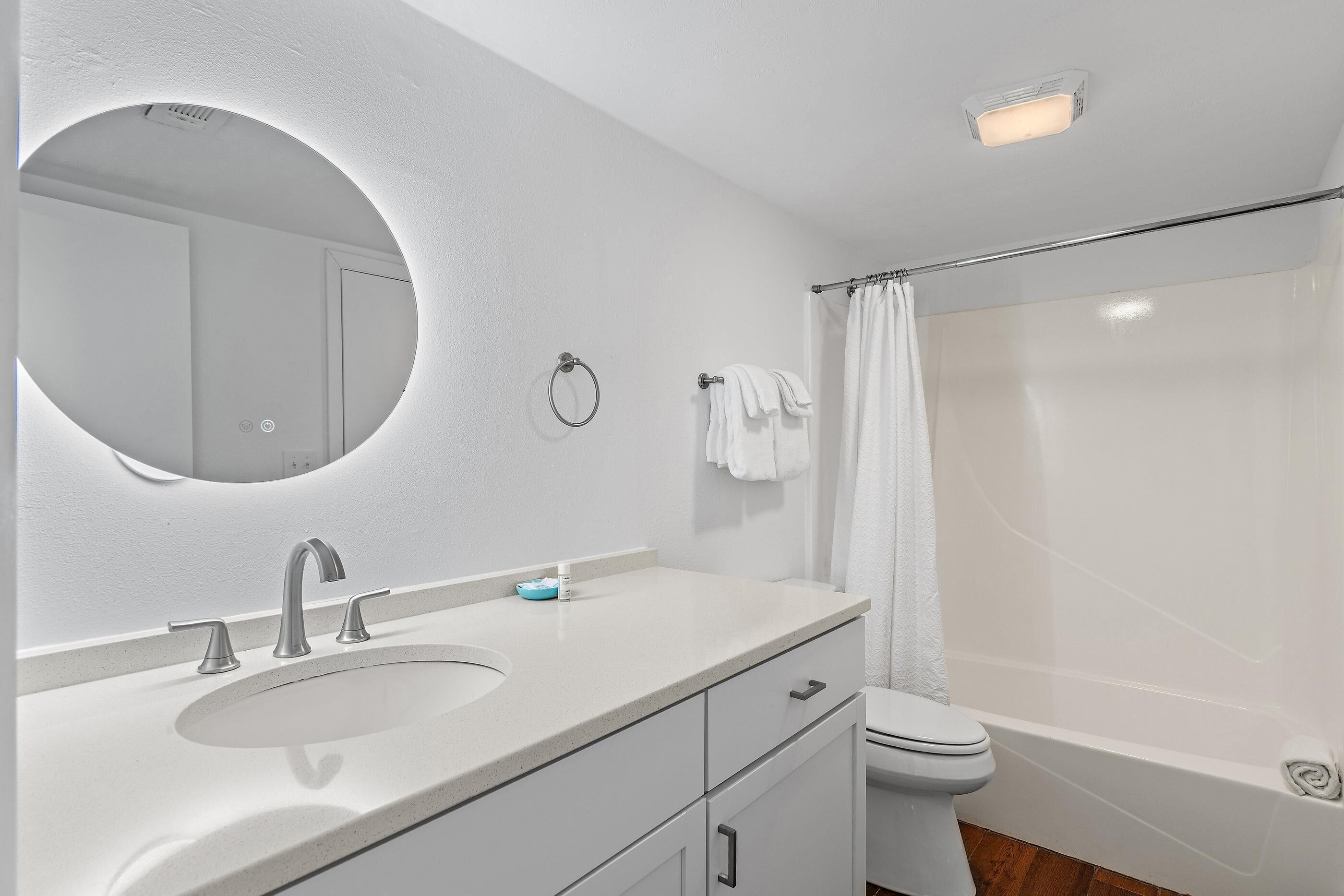 A bathroom with a white sink, mirror, toilet, and shower.