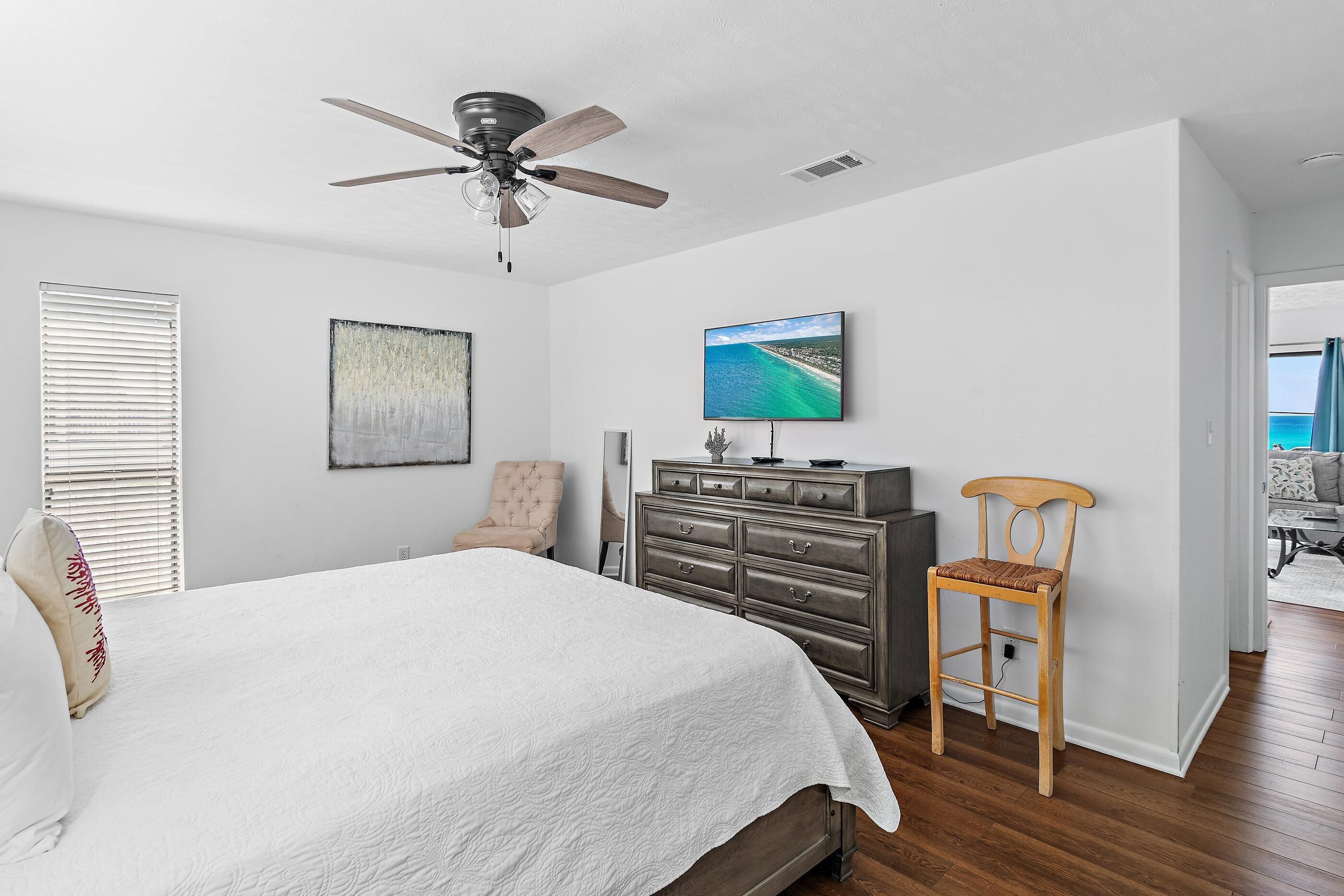 Un dormitorio con una cama, ventilador de techo, cómoda, televisor y una silla.