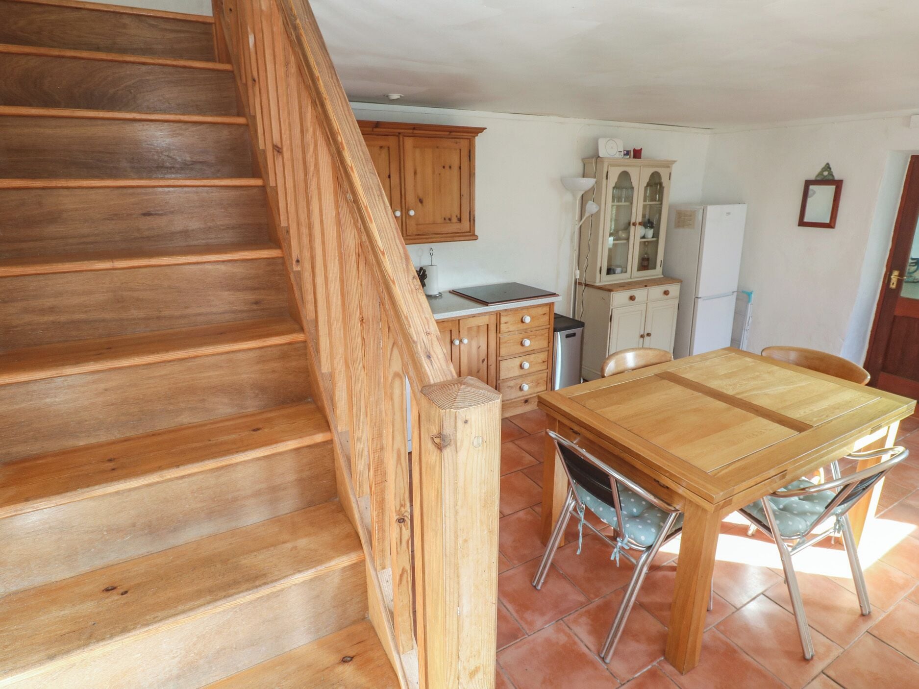 Una escalera de madera que lleva a una cocina con una mesa y sillas para comer.