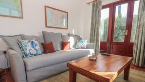 A living room with a sofa, a wooden coffee table, a map on the wall, and a door with curtains. - Kernyk (Penzance)