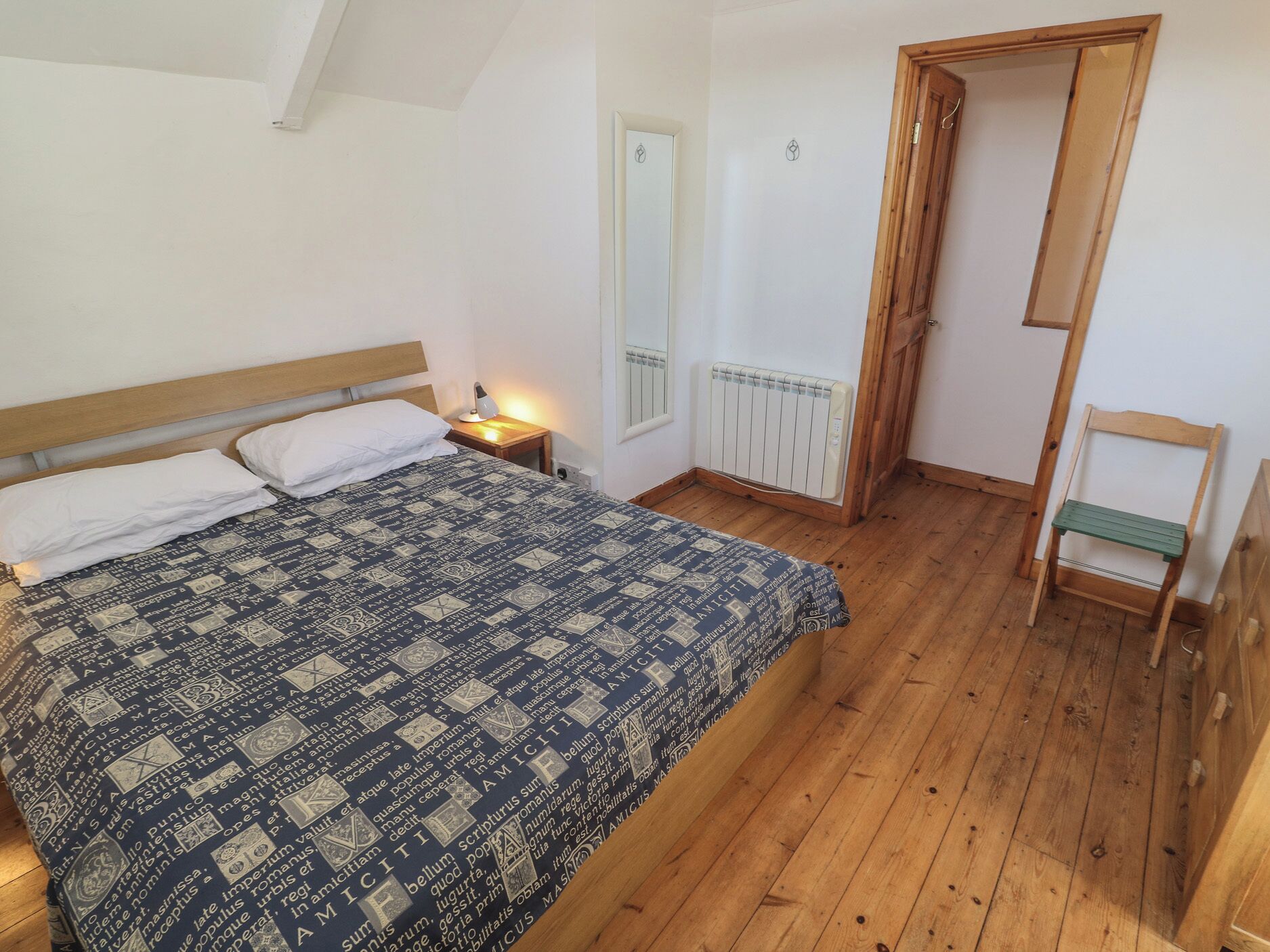 A bedroom with a bed, a nightstand, a radiator, a wooden chair, and a door.