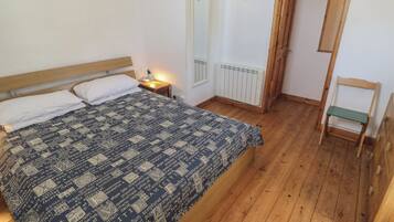 A bedroom with a bed, a nightstand, a radiator, a wooden chair, and a door.