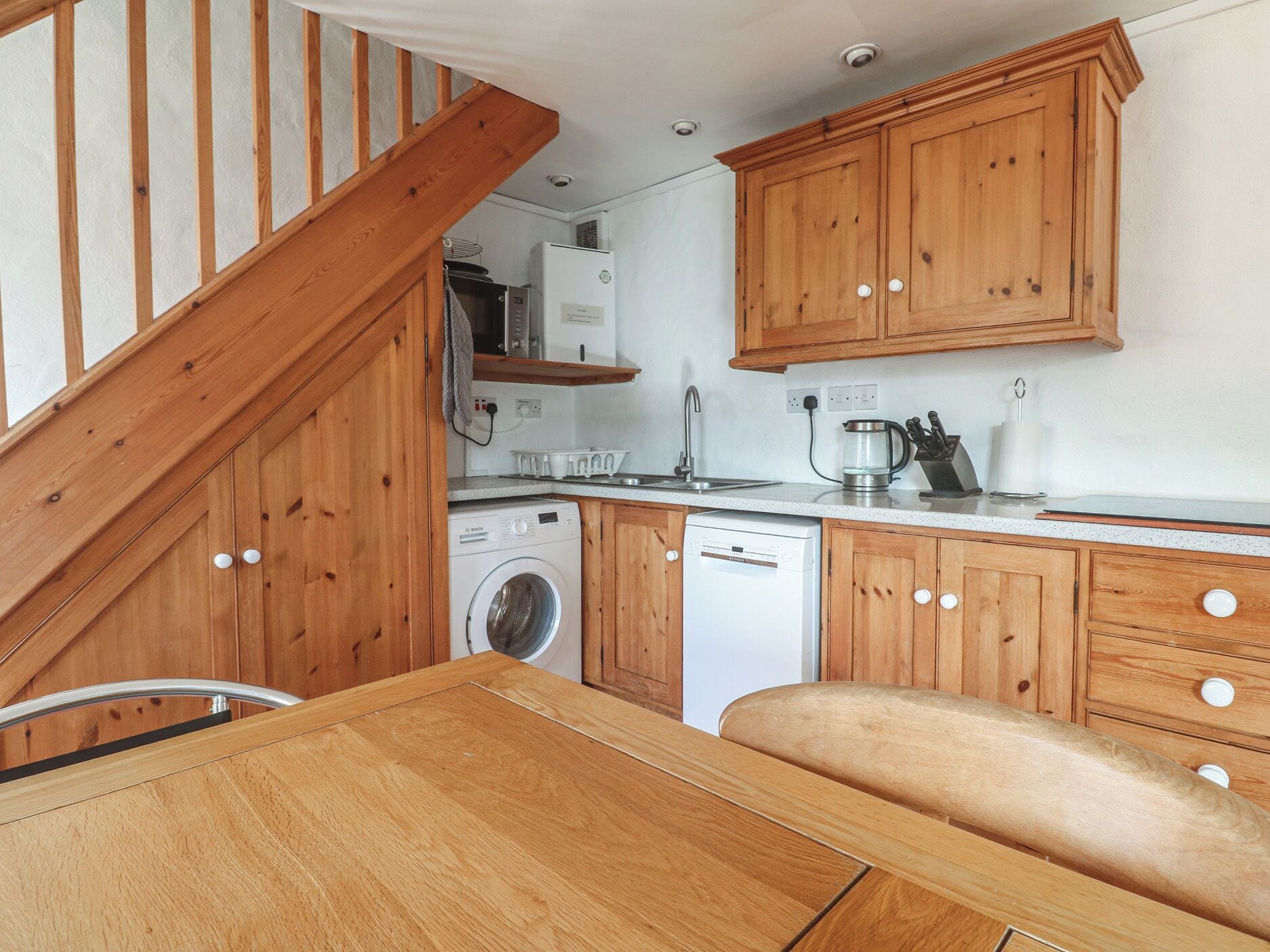 A compact kitchen with wooden cabinets, a washing machine, a dishwasher, and a microwave.