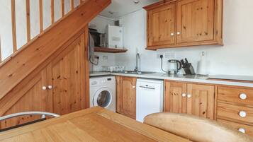 A compact kitchen with wooden cabinets, a washing machine, a dishwasher, and a microwave.