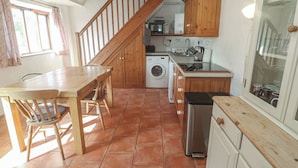 A kitchen with a wooden table, chairs, a washing machine, a microwave, and cabinets. - Kernyk (Penzance)