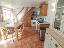 Una cocina con mesa de madera, sillas, lavadora, microondas y armarios.