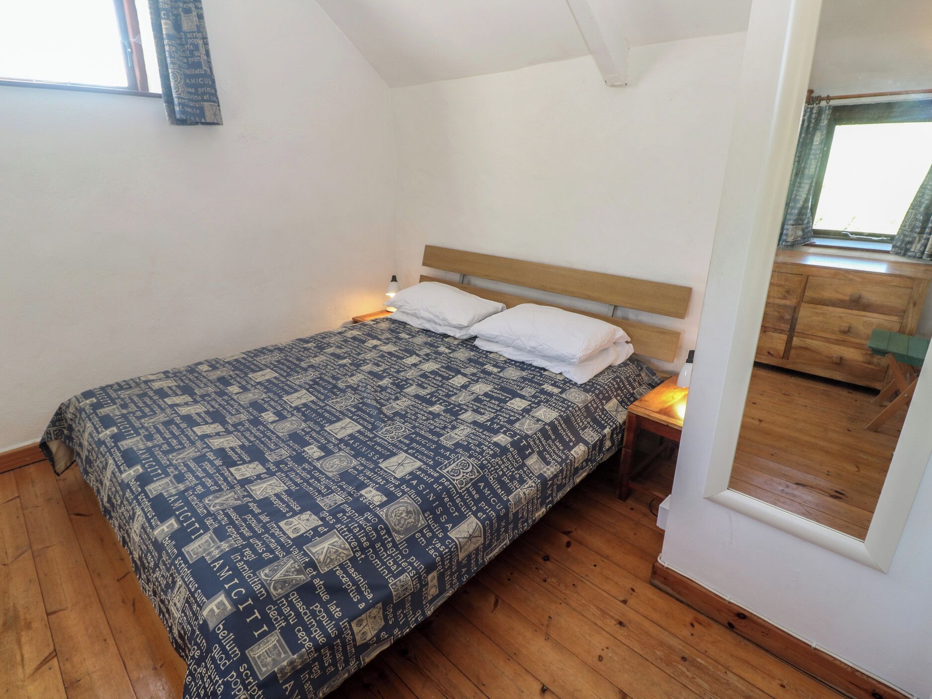 Un dormitorio con una cama, cabecera de madera, mesitas de noche, una ventana y un espejo.