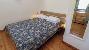 Un dormitorio con una cama, cabecera de madera, mesitas de noche, una ventana y un espejo.
