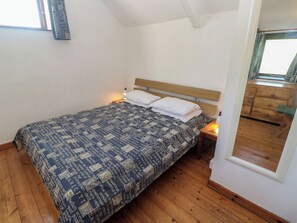 Ein Schlafzimmer mit einem Bett, einem Holzkopfende, Nachttischen, einem Fenster und einem Spiegel.