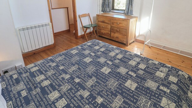 A bedroom with a wooden dresser, a chair, a radiator, and a window with curtains. - Kernyk (Penzance)