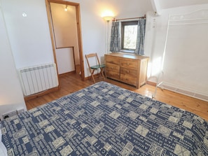 A bedroom with a wooden dresser, a chair, a radiator, and a window with curtains. - Kernyk (Penzance)
