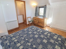 Un dormitorio con un aparador de madera, una silla, un radiador y una ventana con cortinas.