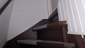 A staircase with wooden steps and a handrail, leading to a landing with a white wall and a door.