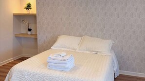 Un letto rifatto con un piumone bianco testurizzato, un comodino con una pianta in vaso e una parete decorata.
