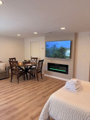A modern living room with a dining area, a flat-screen TV mounted on the wall, and a fireplace.