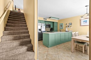 Eine Treppe führt zu einer Küche mit grünen Schränken, einem Kühlschrank und einem Essbereich mit Tisch und Stühlen.