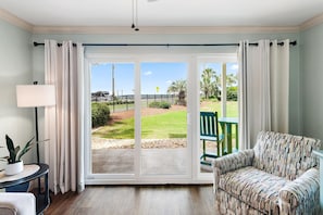 A room with a sliding glass door leading to a patio, a green chair, a patterned sofa, a lamp, and a potted plant. - Ciboney 1001 (Miramar Beach)